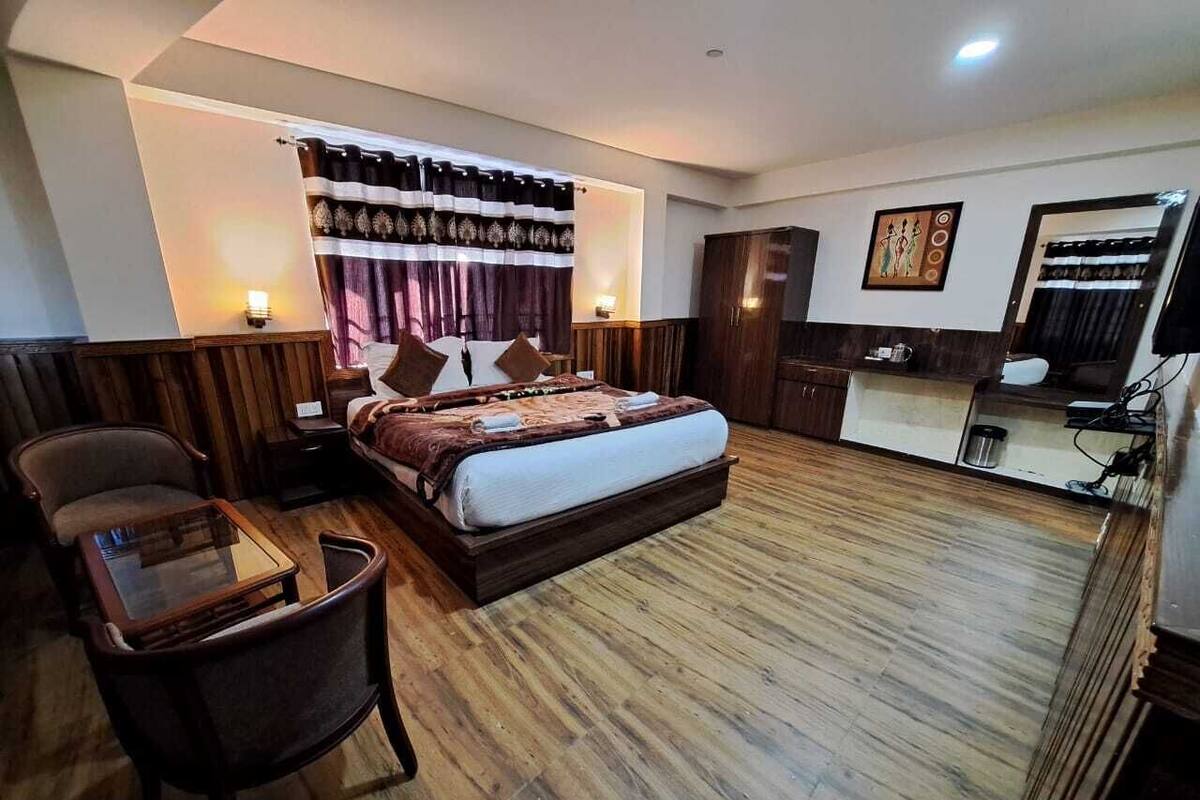 A hotel room with a large bed, a desk, a chair, a wardrobe, and a television.
