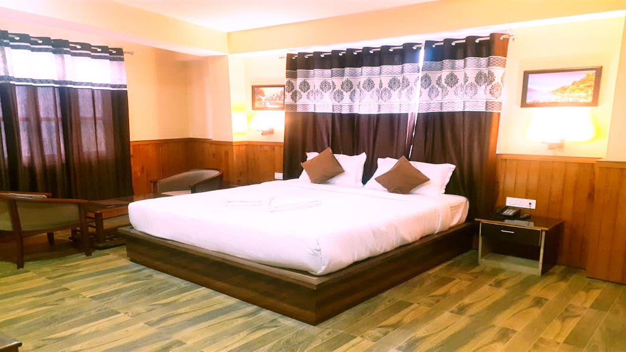 A hotel room with a large bed, wooden headboard, two bedside tables, a desk, and a chair.