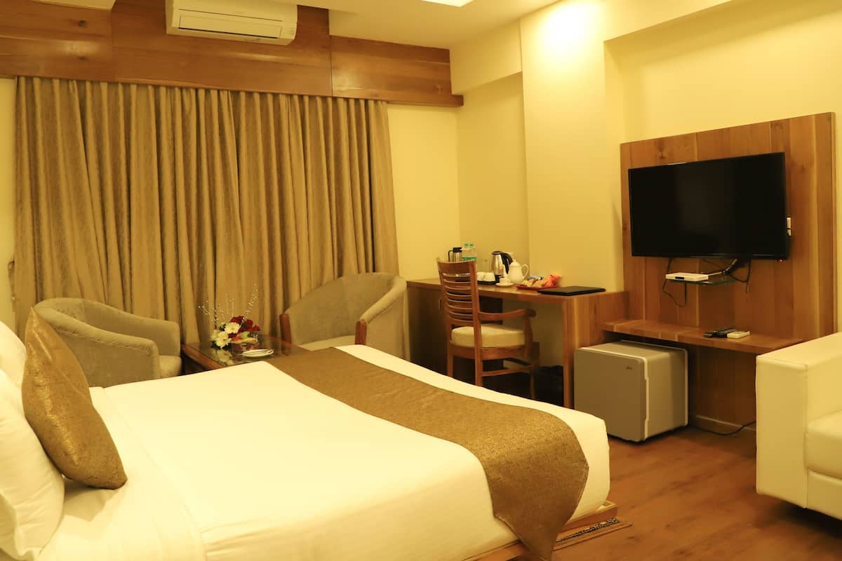 A hotel room with a bed, a desk, a chair, a television, and a small refrigerator.