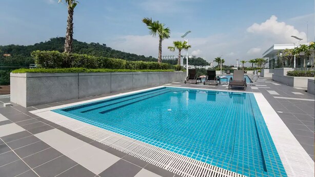 A rectangular swimming pool with a tiled deck, surrounded by palm trees and a landscaped area. - Suria Next To Desa ParkCity (Kuala Lumpur)