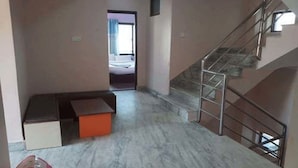 A hallway with a marble floor, a staircase with metal railings, and a bed visible through an open door.