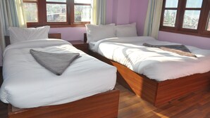 A room with two wooden beds, white bedding, and large windows with curtains.