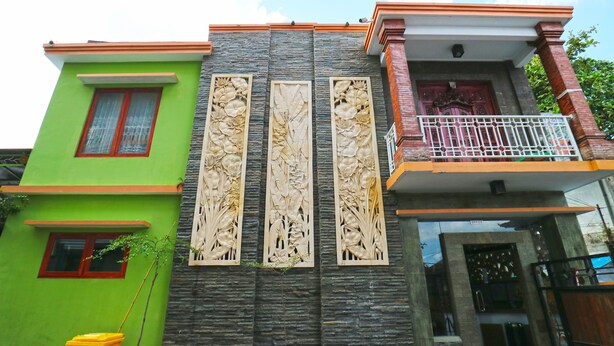 A multi-story building with a green facade, a balcony with a metal railing, and a decorative wall with vertical panels.