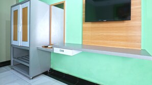 A room with a built-in refrigerator, a wooden cabinet, a flat-screen TV mounted on a wooden panel, and a white countertop.
