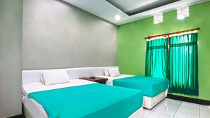 A hotel room with two beds, a nightstand, a window with green curtains, and a green wall.