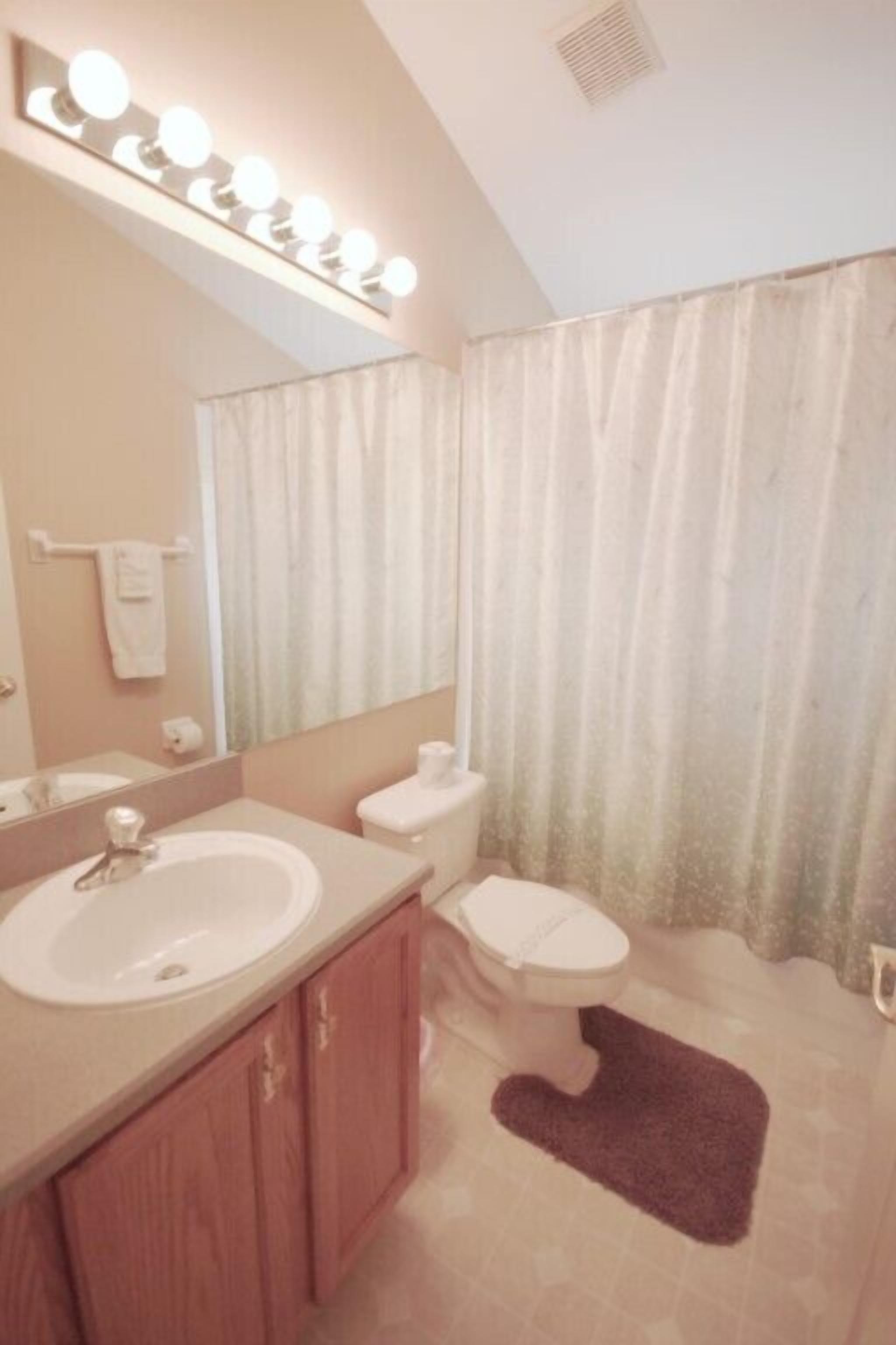 A bathroom with a sink, mirror, vanity, toilet, and shower curtain.