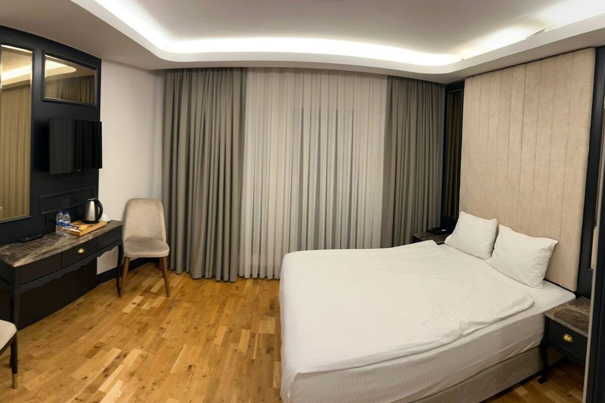 Quarto de hotel com uma cama grande, uma escrivaninha com cadeira, televisão e guarda-roupa.