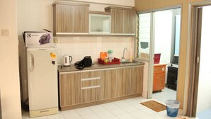 A compact kitchen with a refrigerator, microwave, and sink. There is a small countertop with a kettle, a basket, and a dish rack. - Aman Dua Apartment by SYNC (Batu Caves)