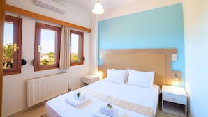 A hotel room with a large bed, two bedside tables, a nightstand, a window with curtains, and an air conditioning unit. - Island Suites (Apokoronas)