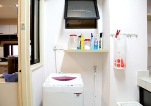 Un cuarto de lavandería con lavadora, un estante con productos de limpieza y un perchero para toallas.