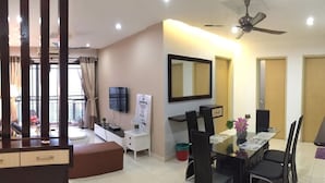 A modern hotel room with a dining area, a flat-screen TV, a ceiling fan, and a large window with curtains. - Casa Indah by SYNC (Petaling Jaya)