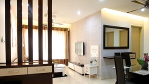 A modern hotel room with a large bed, a desk with a flat-screen TV, a dining area with a table and chairs, and a large mirror on the wall. - Casa Indah by SYNC (Petaling Jaya)