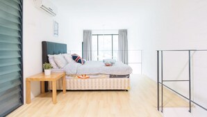 Un dormitorio con cama, una mesita de noche con una planta, una ventana con cortinas y una barandilla de balcón.
