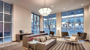 A modern hotel lobby with a sofa, chairs, a desk, and large windows offering views of the outside. - TownePlace Suites by Marriott Salt Lake City Downtown (Salt Lake City)