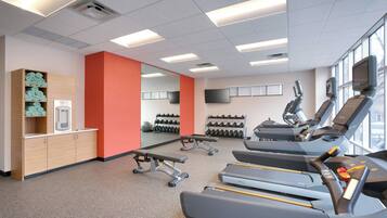 Une salle de sport équipée de tapis de course, de bancs de musculation et d’un mur recouvert de miroirs.