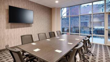 Une salle de conférence avec une longue table, des chaises, un téléviseur à écran plat et de grandes fenêtres.