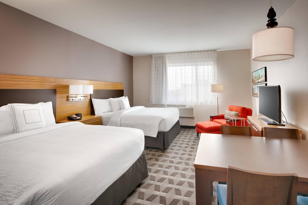 A hotel room with two beds, a desk, a TV, and a window with curtains.