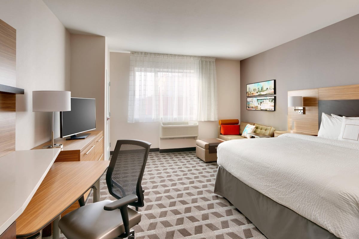 A hotel room with a bed, desk, chair, television, and artwork on the wall.