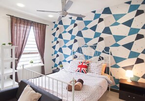 Un dormitorio con una pared de estampado geométrico, una cama con cabecera blanca, un ventilador de techo y una ventana con cortinas.