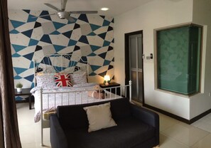 Un dormitorio con pared de diseño geométrico, cama con almohada de la bandera del Reino Unido, sofá negro y una ventana grande.