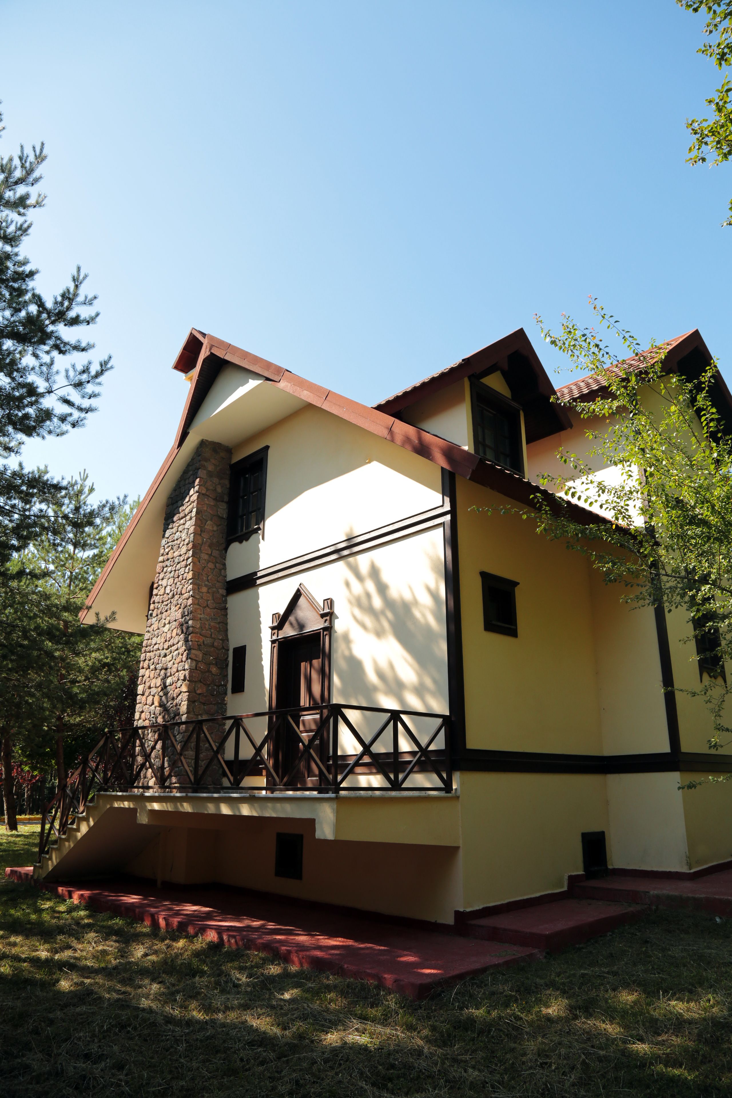 A two-story house with a stone chimney, a balcony, and a red door.