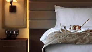Una cama bien hecha con una almohada blanca y una manta gris, una mesita de noche con una lámpara y una pequeña bandeja con una taza y una cuchara.