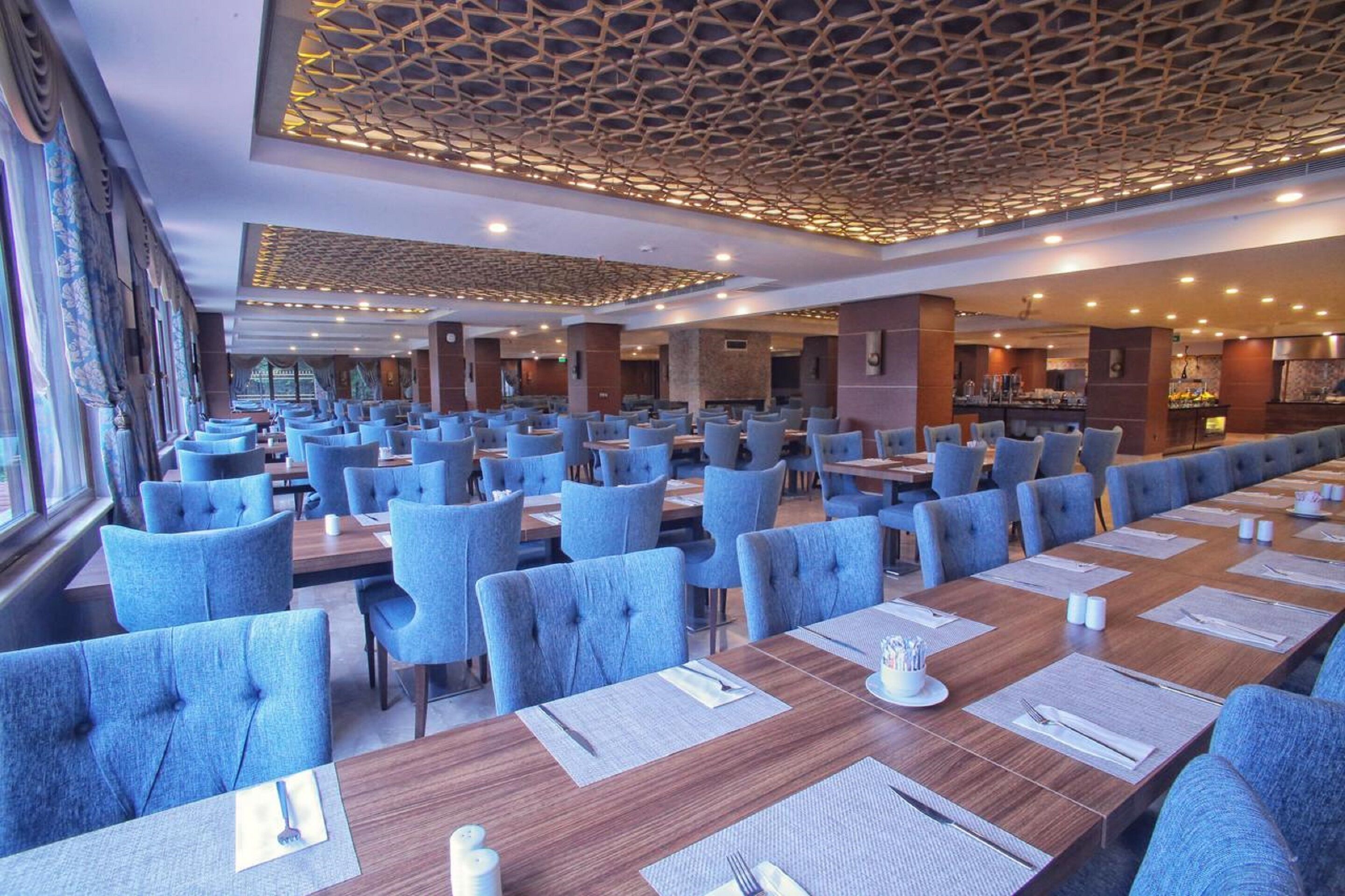 Un restaurante espacioso con sillas de respaldo alto, largas mesas de madera y un techo con diseño.