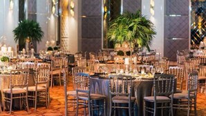 A banquet hall with round tables set for dining, surrounded by chairs.