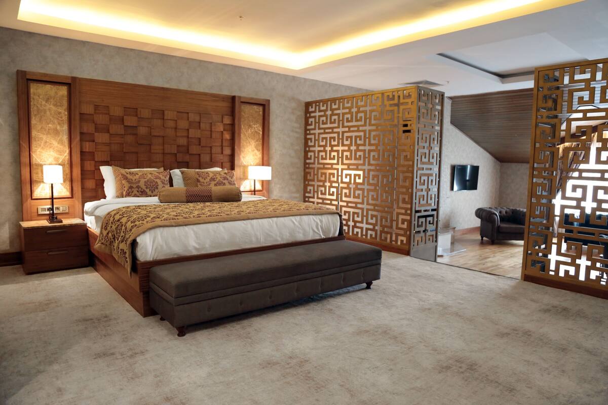 A bedroom with a large bed, bedside tables, a bench, and a decorative partition.