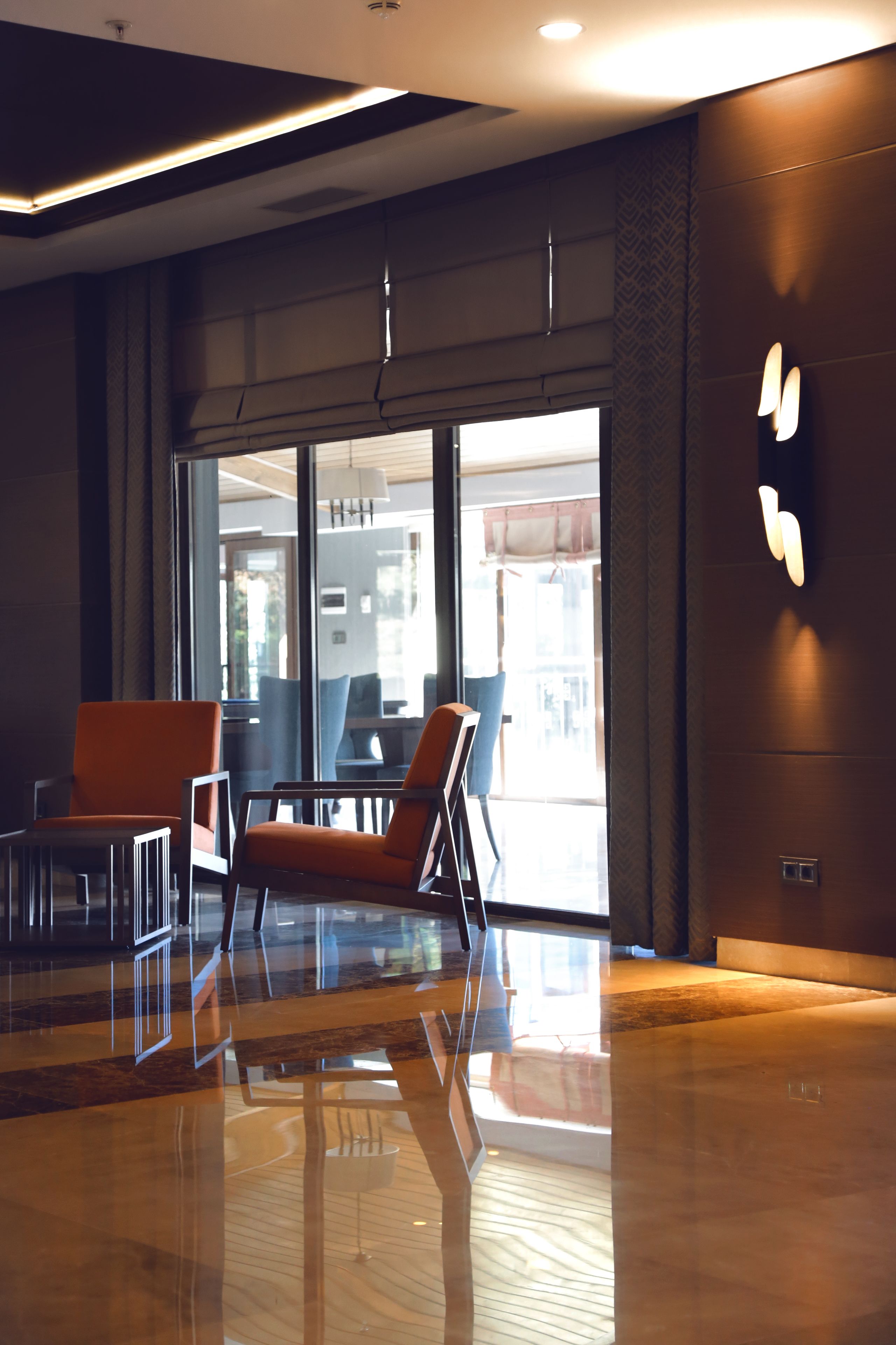 Un moderno vestíbulo de hotel con piso de madera pulida, una zona de estar con sillas anaranjadas y un amplio ventanal que da al comedor.