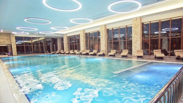 An indoor swimming pool with multiple lounge chairs and a stone wall.