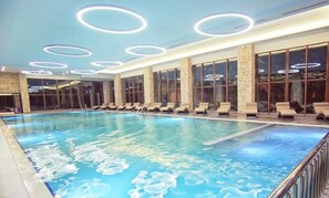 Una piscina interior con múltiples sillones de descanso y una pared de piedra.