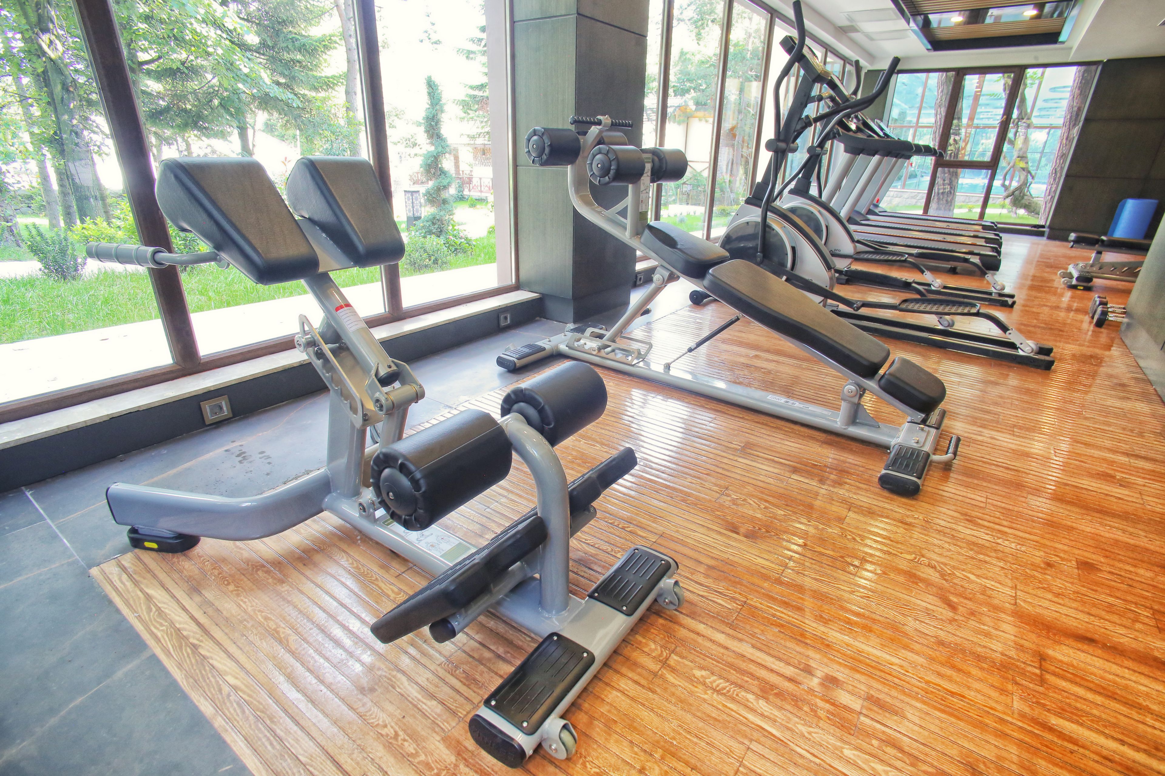Une salle de sport équipée de divers appareils d’exercice, dotée de grandes fenêtres et d’un plancher en bois.