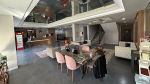 A spacious, modern living area with a high ceiling, a dining table with chairs, a sofa, and a staircase leading to an upper level. - On Hotel (Antalya)