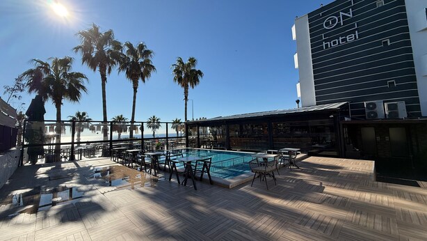 A rooftop pool area with palm trees, a bar, and a hotel building in the background. - On Hotel (Antalya)