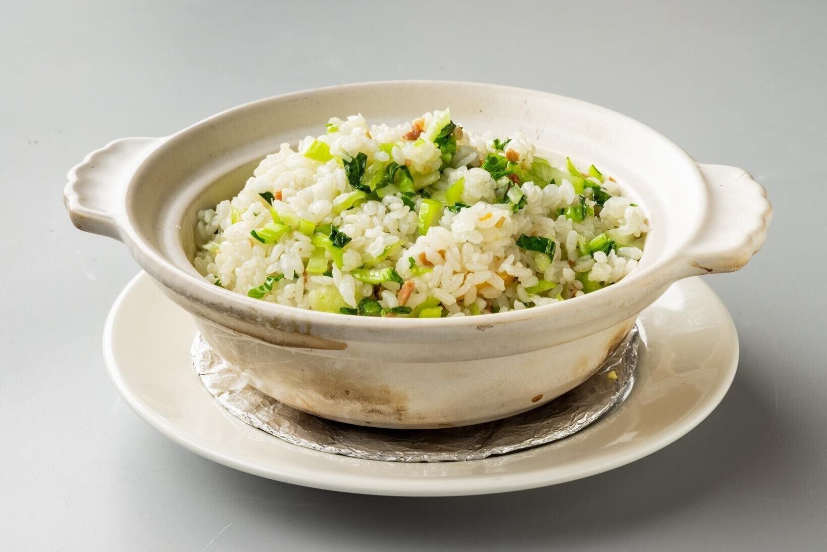 A white ceramic bowl filled with rice and green vegetables on a white plate.