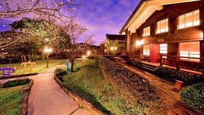 A well-lit building with a wooden facade, a pathway leading to the entrance, and a small garden area with trees and shrubs. - Yanmin Hot Spring Resort (Taipei)