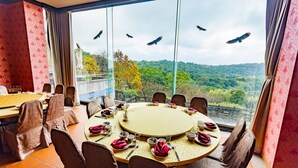 A dining room with a round table set for six, large windows with a view of a forested landscape, and a balcony railing. - Yanmin Hot Spring Resort (Taipei)
