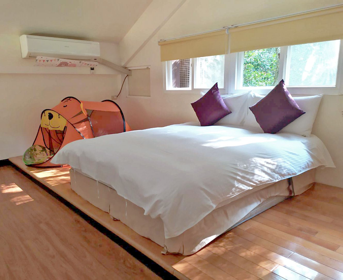 Ein Schlafzimmer mit Bett, Kissen, einem Fenster und einer Klimaanlage.