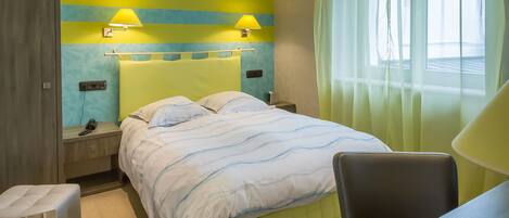 A hotel room with a bed, bedside tables, a chair, a desk, and a window with curtains.