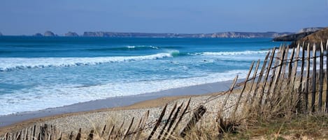 Escena de playa costera con una valla de madera en primer plano y acantilados rocosos al fondo.