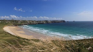 A coastal landscape with a sandy beach, grassy areas, and a rocky cliff overlooking the ocean. - Hostellerie de la Mer (Crozon)