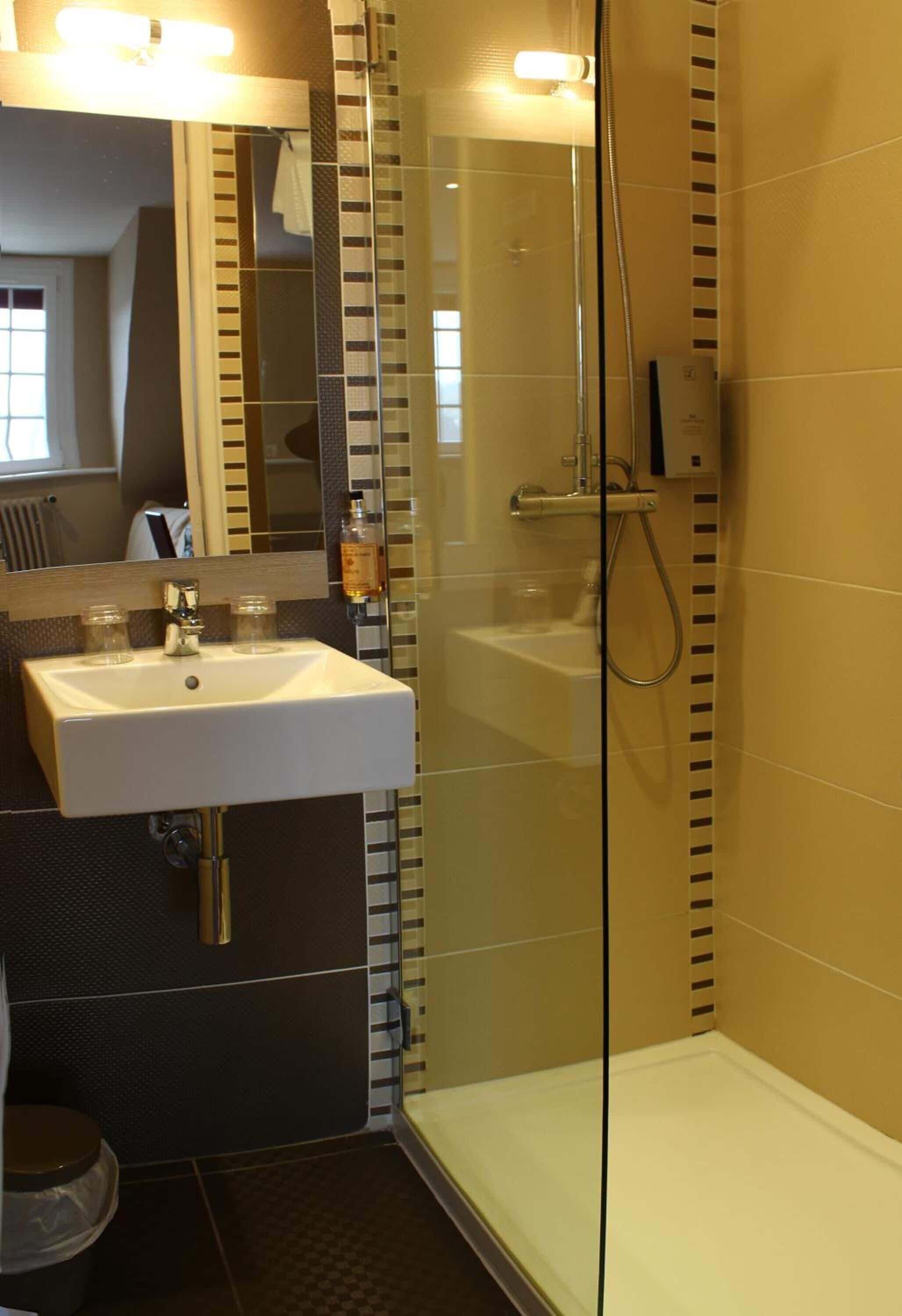 Une salle de bain avec une douche à parois de verre, un lavabo avec un miroir au-dessus et des toilettes.
