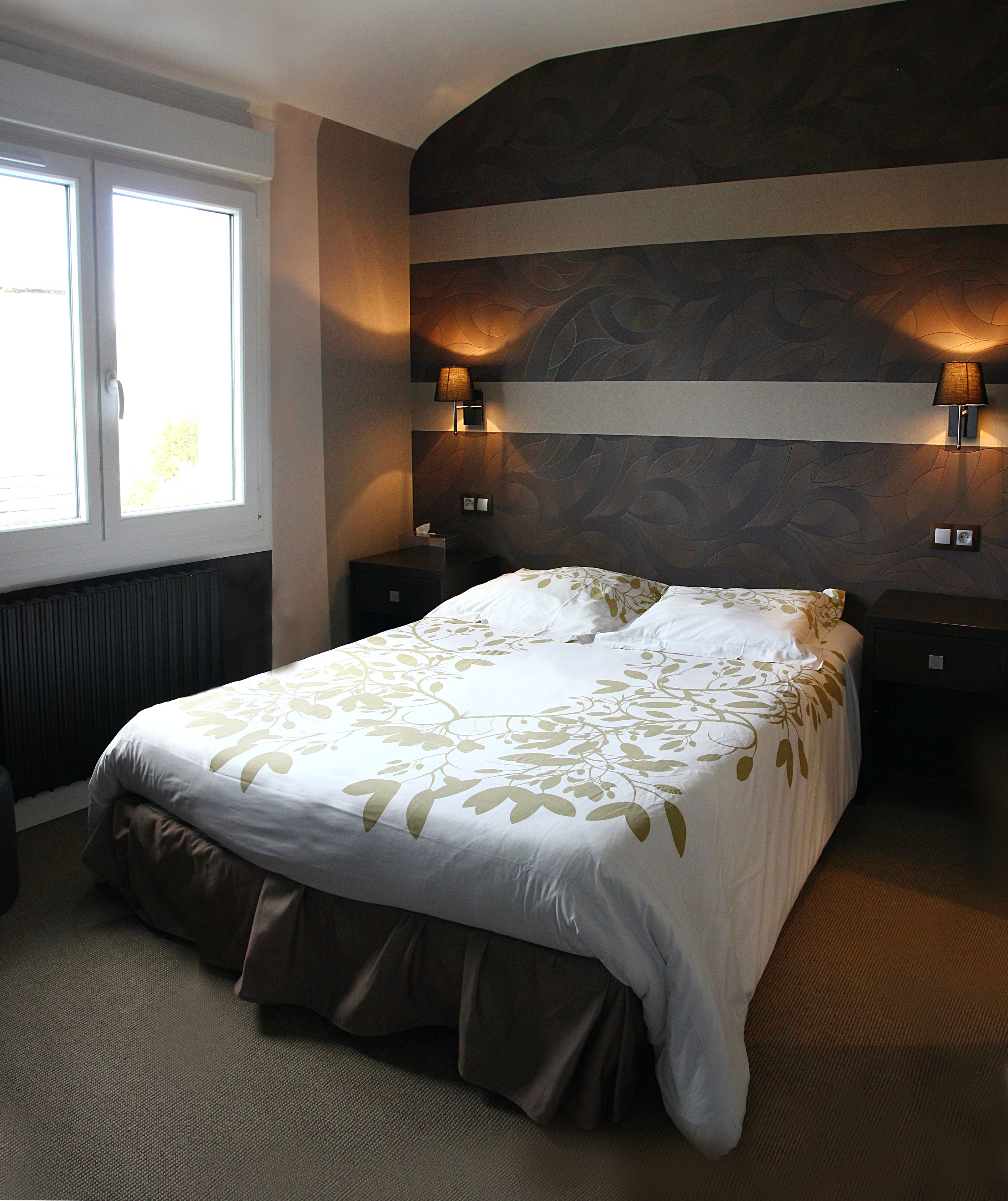 A neatly made bed with a floral bedspread, two bedside lamps, and a window with blinds.