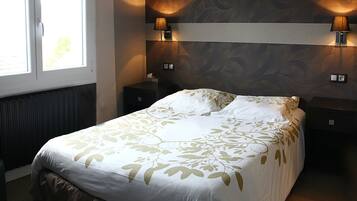 A neatly made bed with a floral bedspread, two bedside lamps, and a window with blinds.