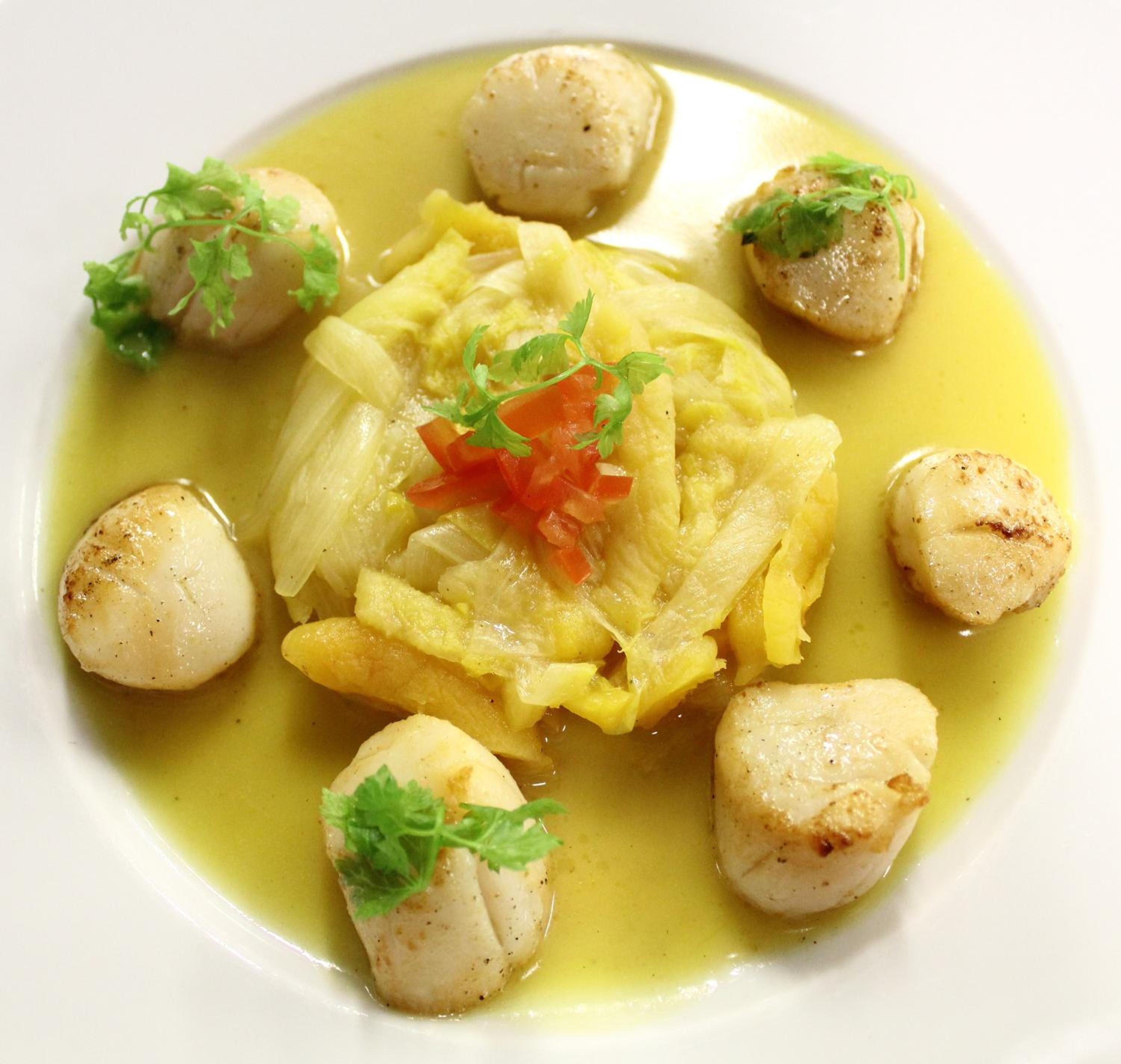 A plate of food with scallops, a central vegetable, and garnishes.