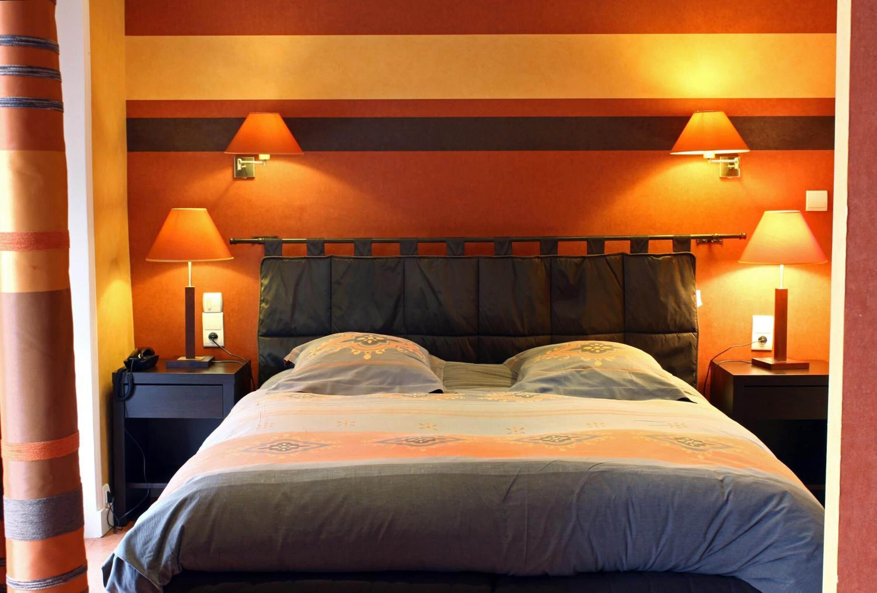 A hotel room with a bed, two bedside lamps, a nightstand, and a wall with a striped pattern.