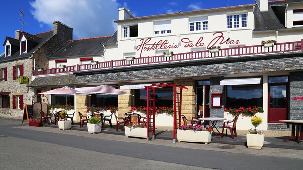A hotel with outdoor seating, a red and white awning, and flower boxes. - Hostellerie de la Mer (Crozon)