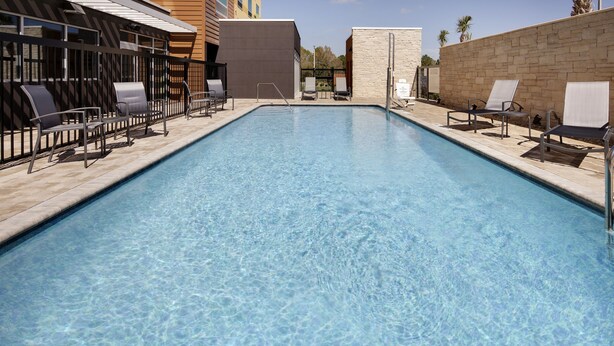 Una piscina rectangular con agua azul cristalina, rodeada de sillones de descanso y un muro de piedra.
