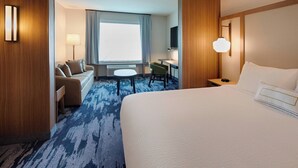 Habitación de hotel con una cama grande, un escritorio, una silla, un sofá, una lámpara y un televisor.